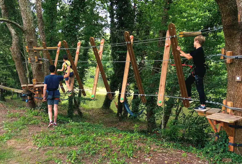 Enfants sur un atelier de l'accrobranche AirParc Périgord en bord de Dordogne, un parent aidant du sol.