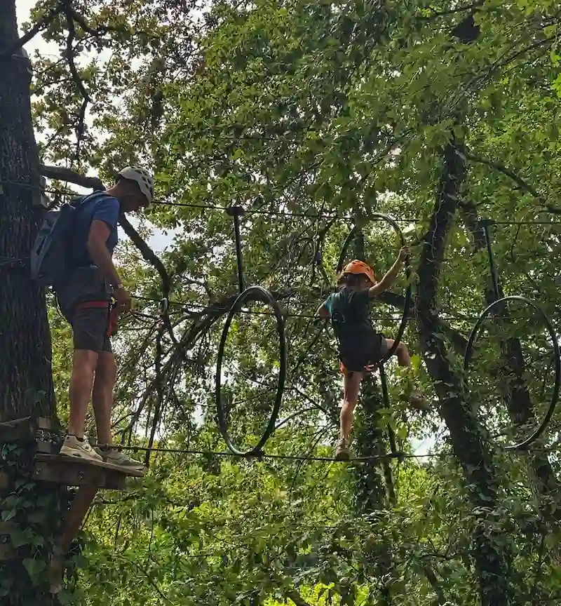 Une famille sur le passage d'un obstacle en anneaux sur le parcours vert de l'accrobranche AirParc Périgord.