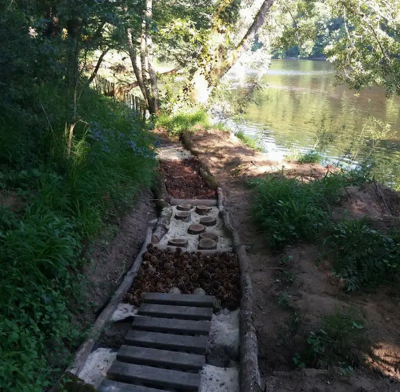 Vue sur le sentier pieds nus d'AirParc Périgord, avec écorces, sable et galets au bord de l'eau.